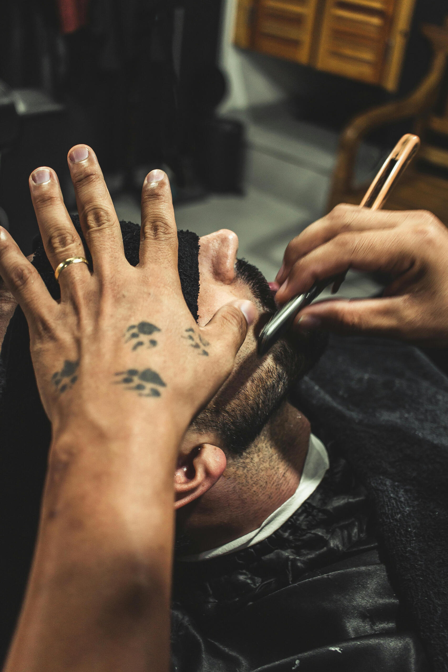 Close-up of a tattooed barber giving a traditional razor shave in a stylish Korean barbershop.